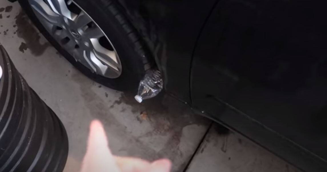 Personne observant une bouteille près de sa voiture avec perplexité